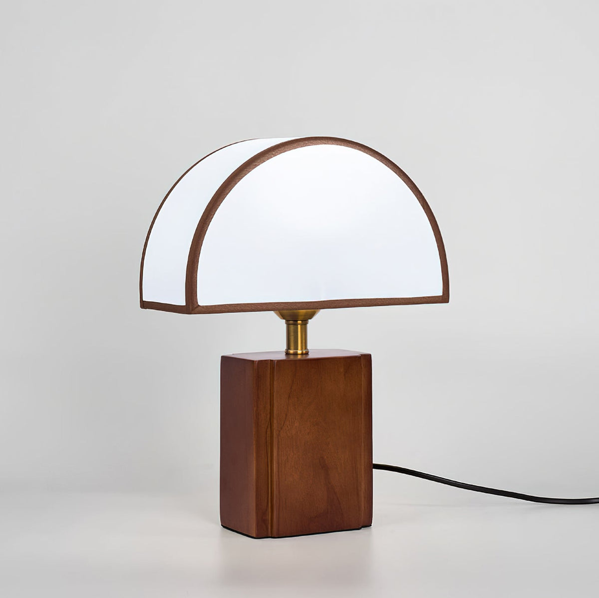 Seen from the front on a pale grey backdrop, a Clérachic table lamp with a half-round white shade and its cord trailing right.