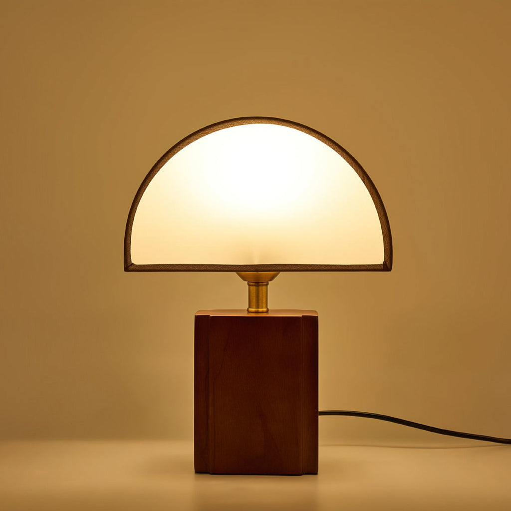 A Clérachic table lamp glowing warmly against an amber backdrop, its half-round shade lit from within.