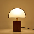 A Clérachic table lamp glowing warmly against an amber backdrop, its half-round shade lit from within.