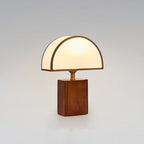 Clérachic walnut and white table lamp, lit, on a soft grey backdrop with a half-round fabric shade.
