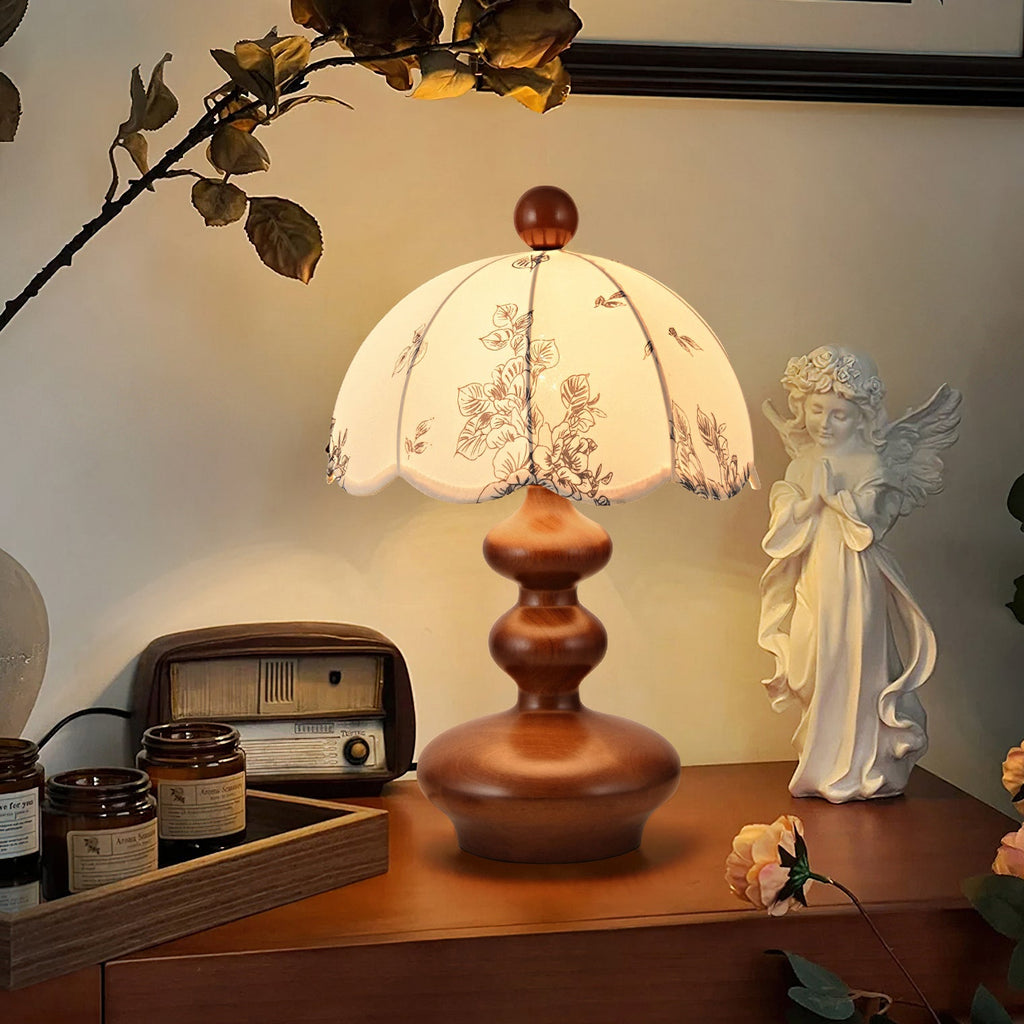 Clérachic table lamp with a rounded, tiered walnut-tone base glowing on a wooden cabinet, with a retro radio and a statuette.