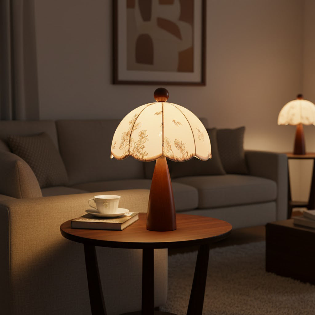 Clérachic lamp with a tapered wooden base lit on a round side table, with a teacup and book, beside a grey sofa.