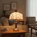 Clérachic lamp with a brass foot and wooden bead stem glowing on a side table, next to an armchair and a teacup.