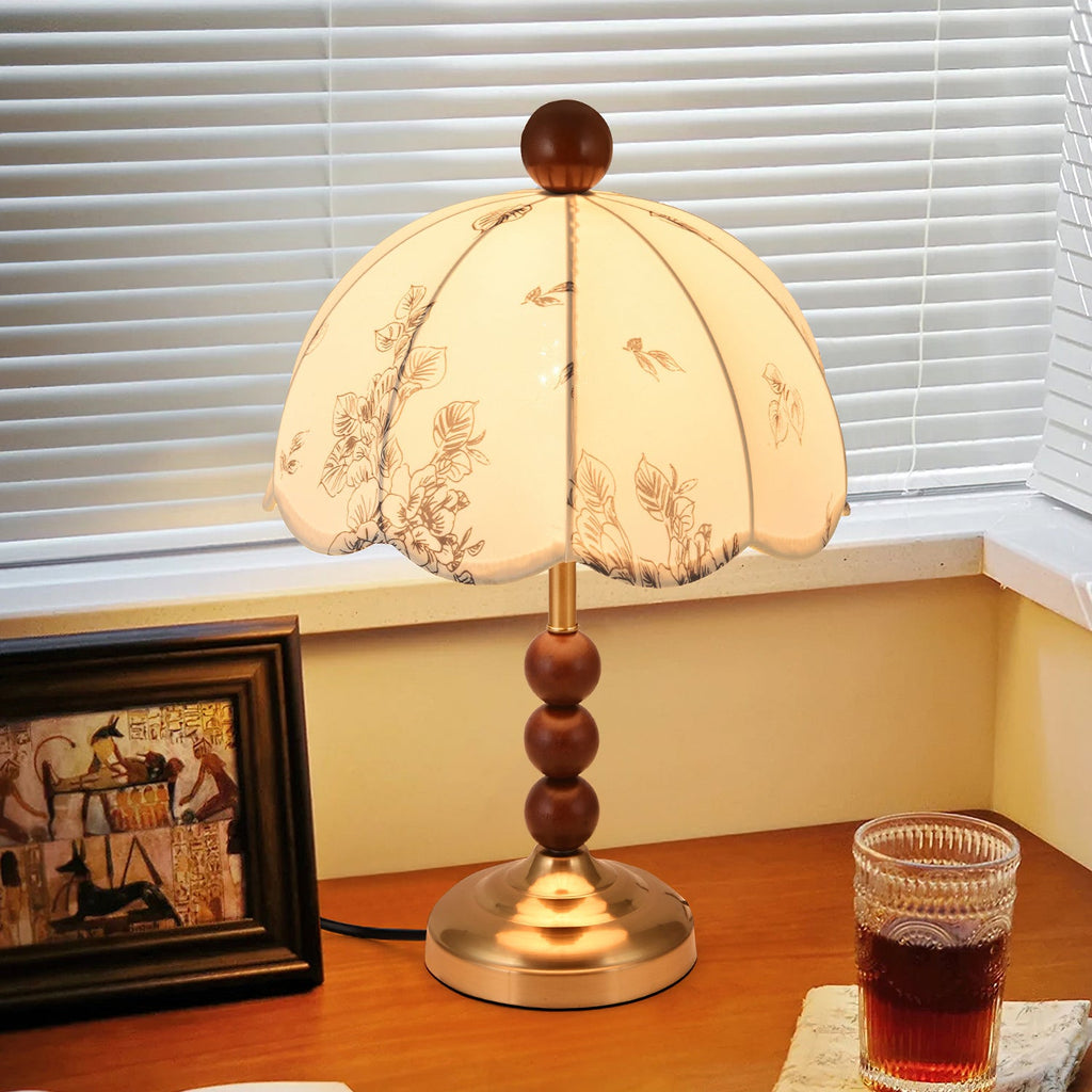 Close view of a lit Clérachic lamp with a brass foot and wooden bead stem, beside a framed picture and a glass of tea.