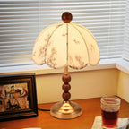 Close view of a lit Clérachic lamp with a brass foot and wooden bead stem, beside a framed picture and a glass of tea.
