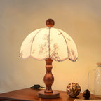 Clérachic lamp with a turned wooden base and floral scalloped shade on a desk, beside a rattan ball and a pine cone.