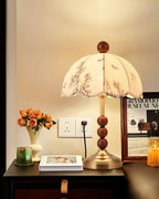 Clérachic lamp with a brass foot and wooden beads on a dark nightstand, beside orange roses in a vase and a framed poster.