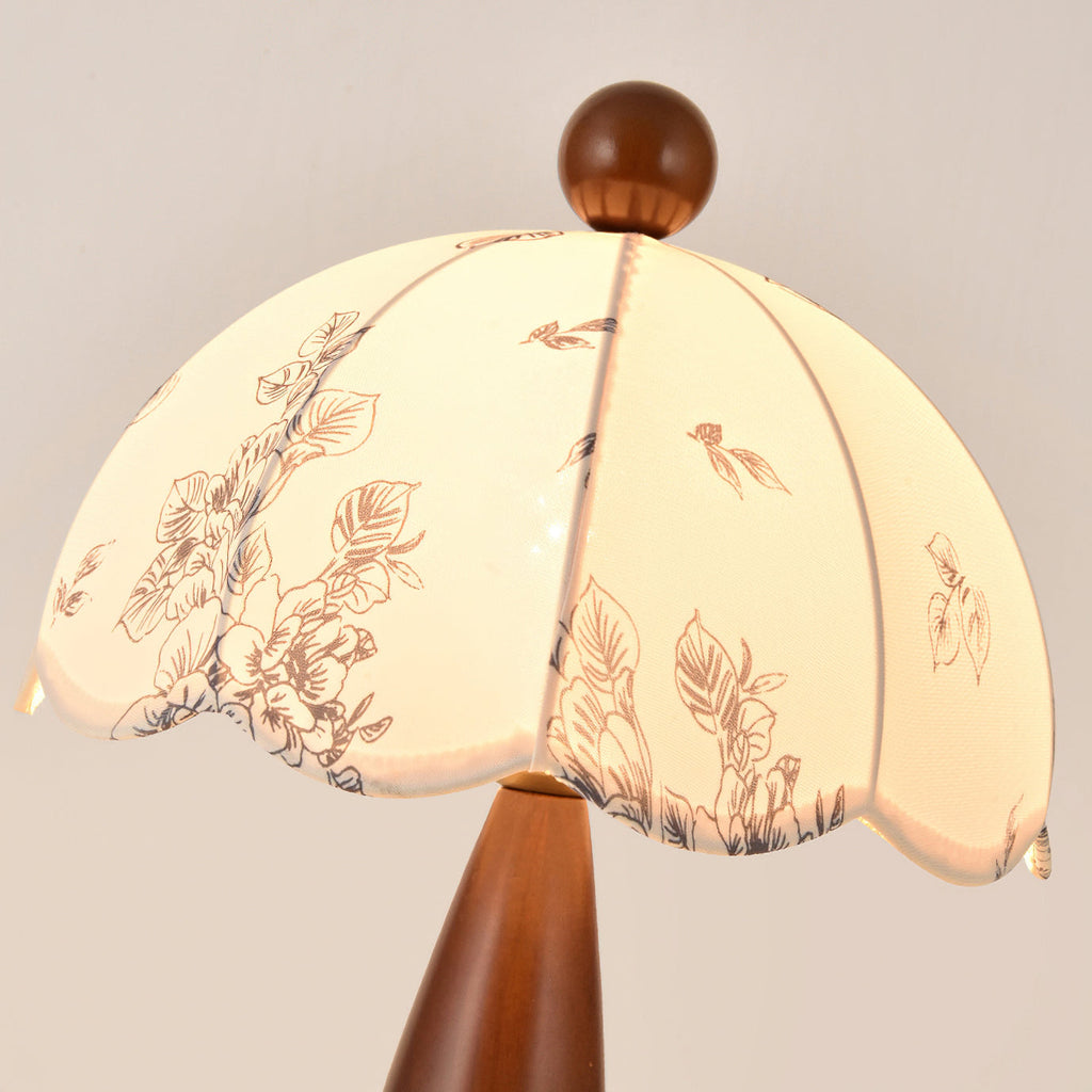 Close view of the scalloped floral-print shade and wooden finial of this Clérachic lamp, lit from within.