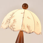 Close view of the scalloped floral-print shade and wooden finial of this Clérachic lamp, lit from within.