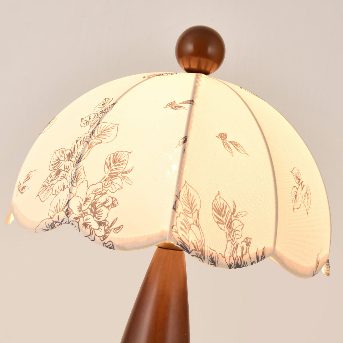 Close view of the scalloped floral-print shade and wooden finial of this Clérachic lamp, lit from within.