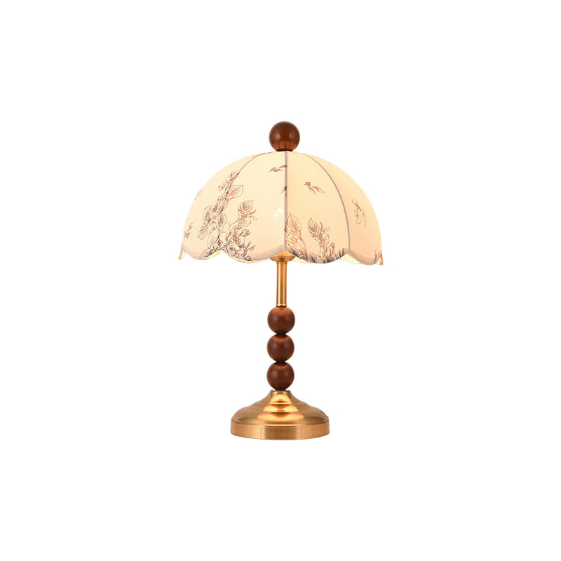 This Clérachic table lamp with a brass foot and three wooden beads under a scalloped floral shade, on a white background.