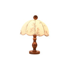 This Clérachic table lamp with a turned wooden stem on a round foot and a scalloped floral shade, on a white background.