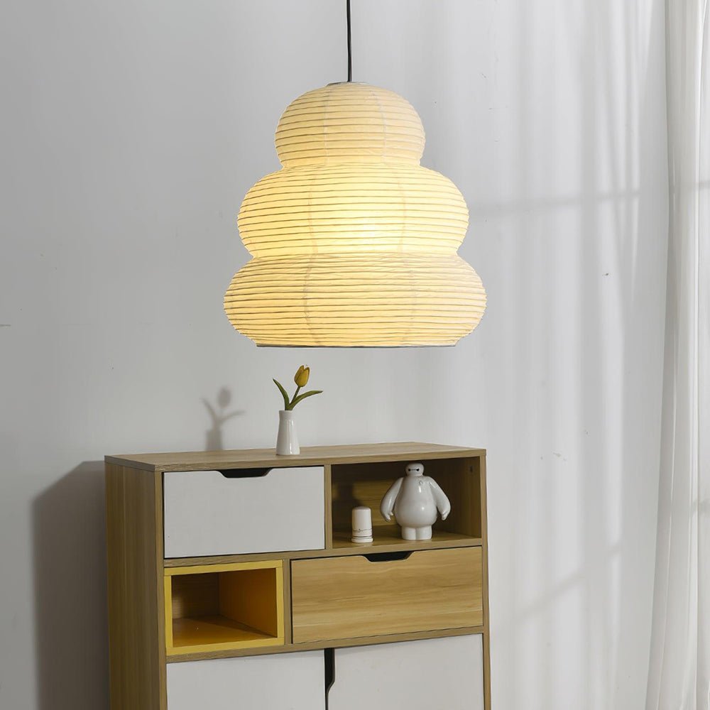 Clérachic tiered paper pendant light glowing above the pale wood sideboard, a small candle and the white figurine set on the open shelf below.