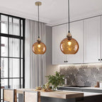 A pair of orange Clérachic water ripple glass globe pendants above a white kitchen island, filaments glowing through the tinted glass.