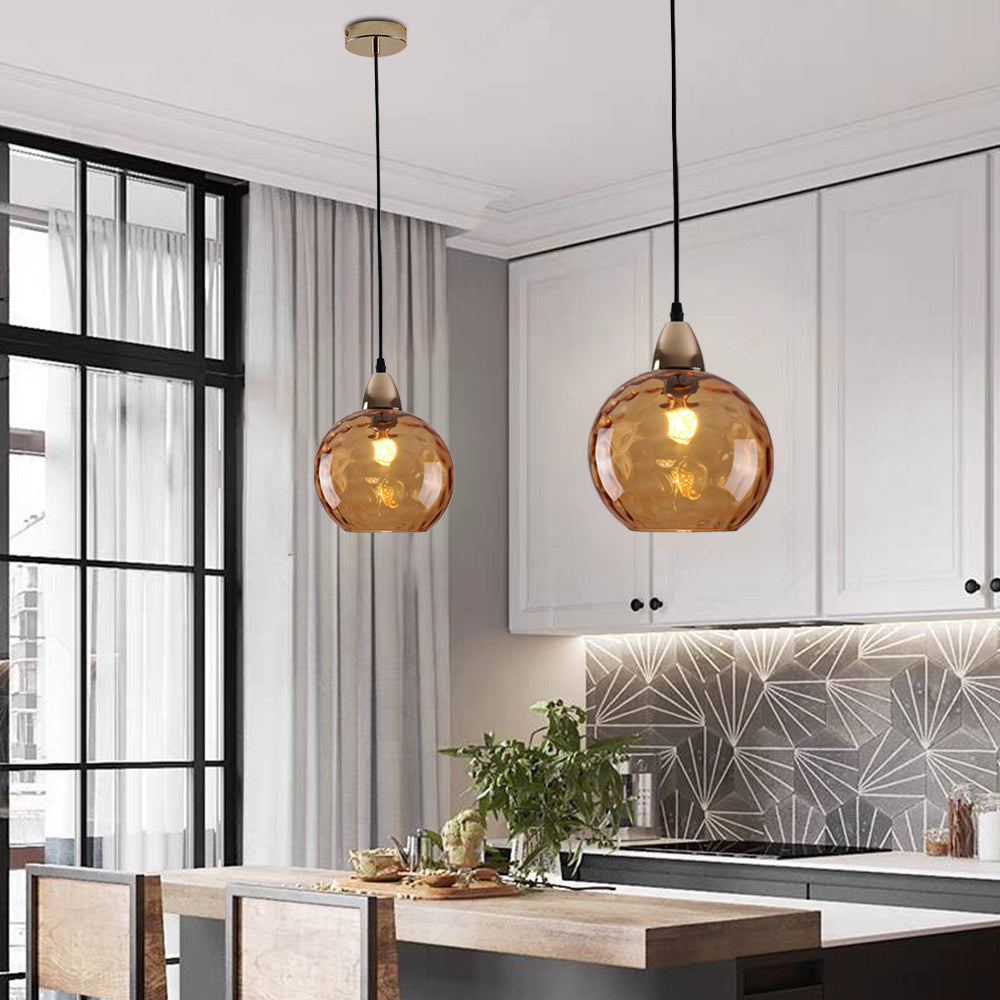 A pair of orange Clérachic water ripple glass globe pendants above a white kitchen island, filaments glowing through the tinted glass.