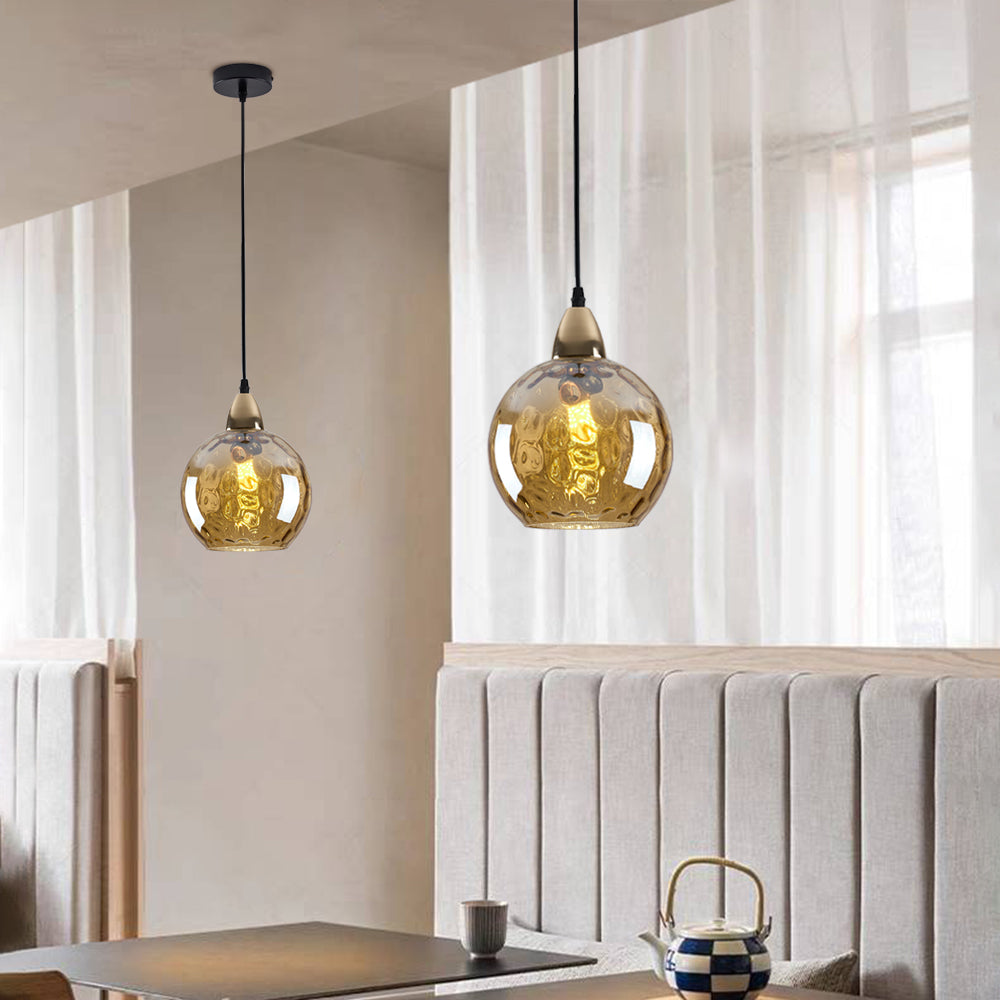 Amber Clérachic water ripple glass globe pendants in a dining corner, the golden glass catching daylight from the curtained window.