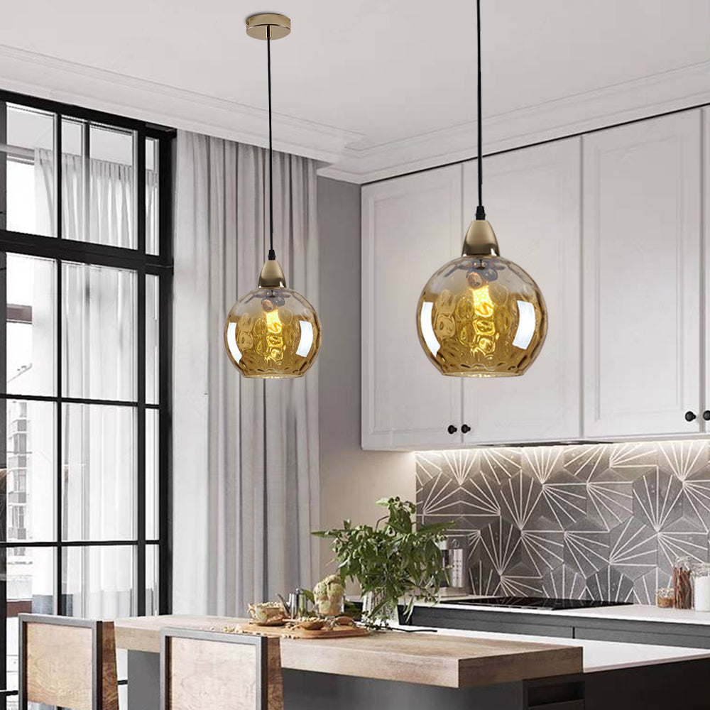 Two amber Clérachic water ripple glass globe pendants lighting a white kitchen, dimpled glass over the worktop and dining table.