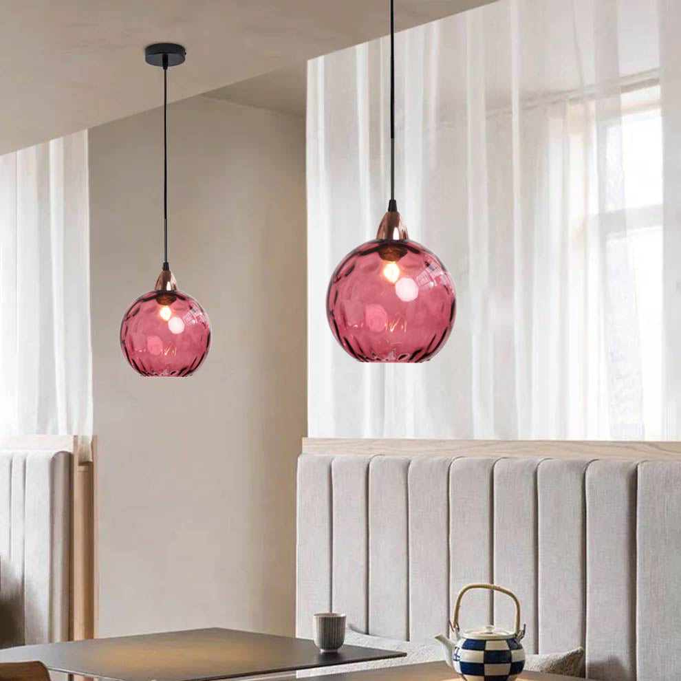 Crimson-pink Clérachic water ripple glass globe pendants above a beige banquette, copper socket cups at the neck of each dimpled globe.