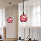 Crimson-pink Clérachic water ripple glass globe pendants above a beige banquette, copper socket cups at the neck of each dimpled globe.