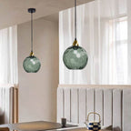 Dark green Clérachic water ripple glass globe pendants hung in pairs over a dining nook, the tinted glass reading almost slate in daylight.