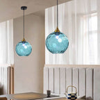 Light blue Clérachic water ripple glass globe pendants at staggered drops in a dining corner, cool tinted glass over a pale banquette.