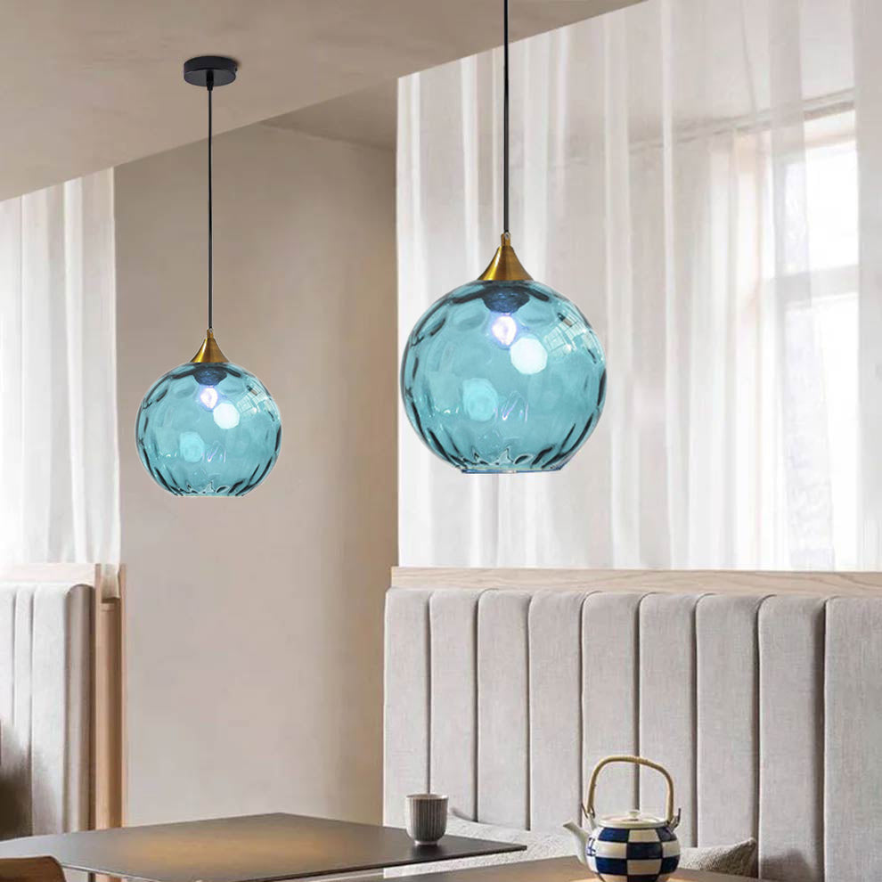 Light blue Clérachic water ripple glass globe pendants at staggered drops in a dining corner, cool tinted glass over a pale banquette.