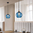 Dark blue Clérachic water ripple glass globe pendants above a dining table, deep tinted glass with a warm filament showing through.