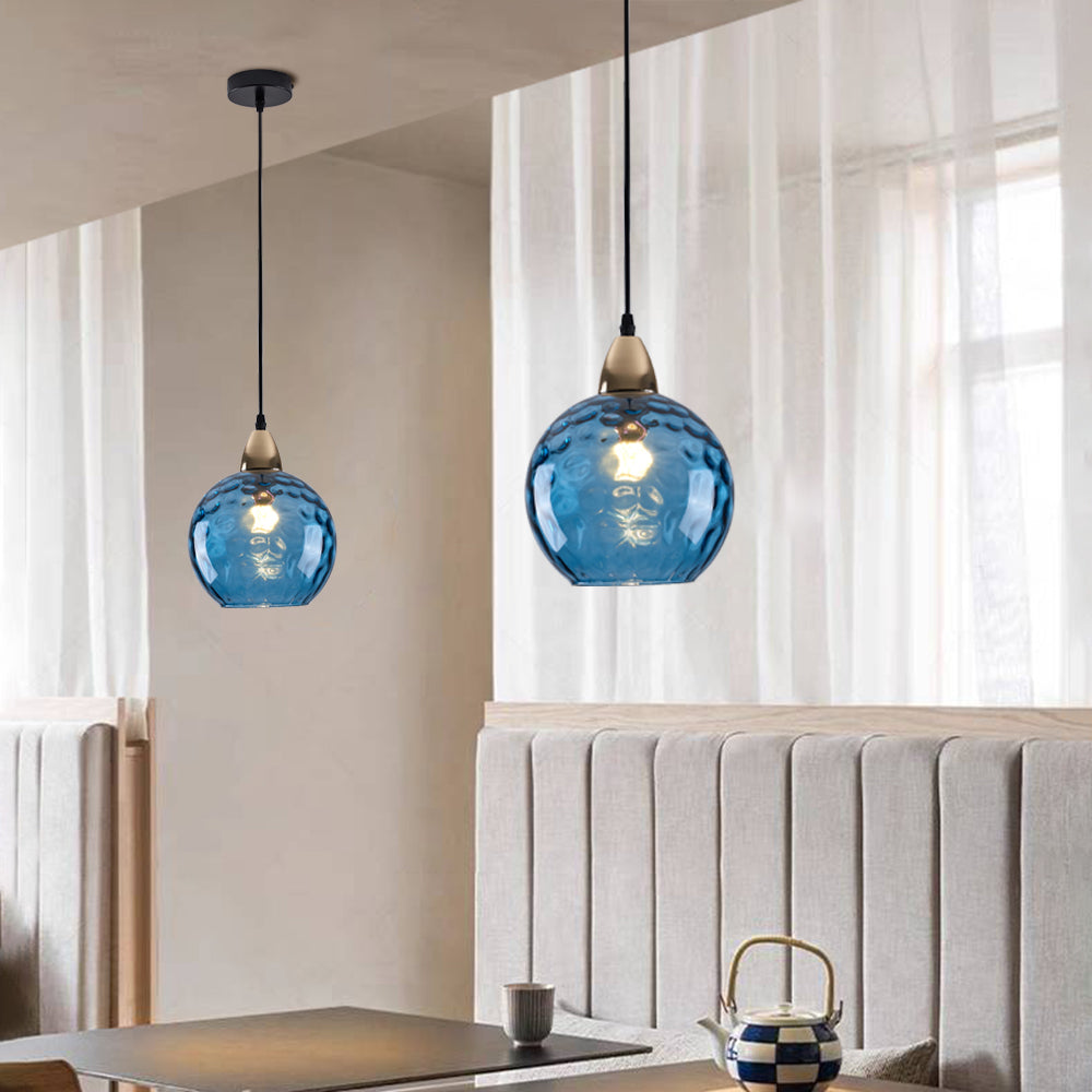 Dark blue Clérachic water ripple glass globe pendants above a dining table, deep tinted glass with a warm filament showing through.