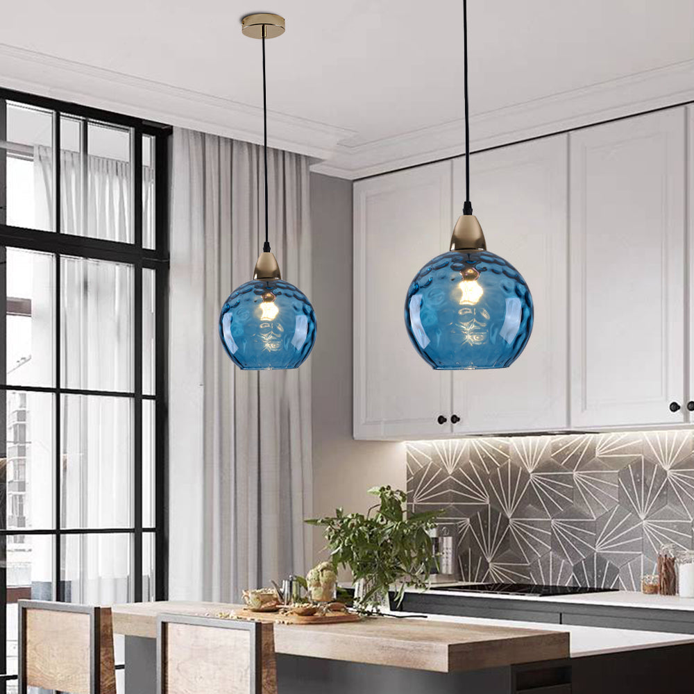 A pair of dark blue Clérachic water ripple glass globe pendants in a white kitchen, hung from a gold ceiling rose over the island.
