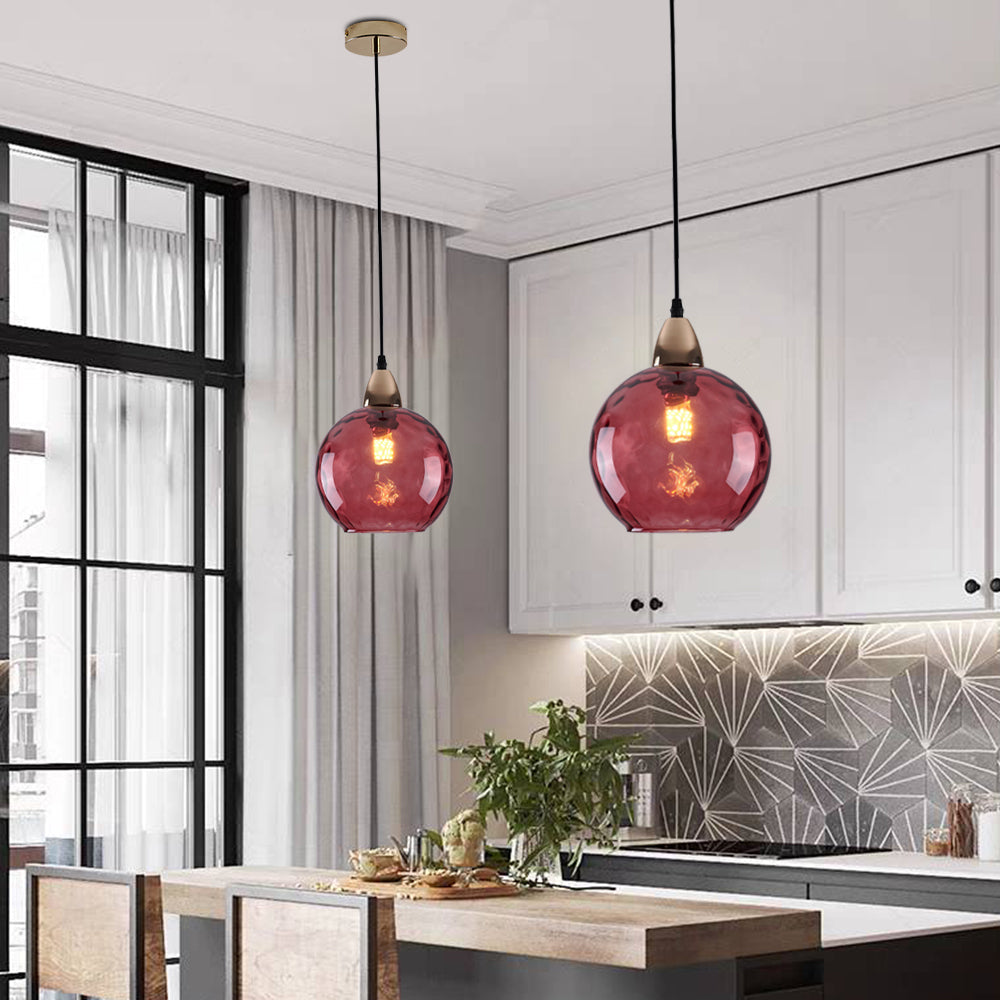 Deep raspberry Clérachic water ripple glass globe pendants in a white kitchen, hung at two heights above the island.