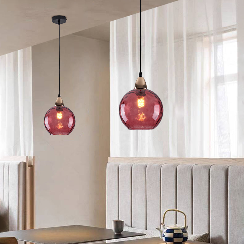 Dusty rose Clérachic water ripple glass globe pendants in a dining corner, the tinted glass lit against a pale plaster wall.