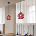 Dusty rose Clérachic water ripple glass globe pendants in a dining corner, the tinted glass lit against a pale plaster wall.