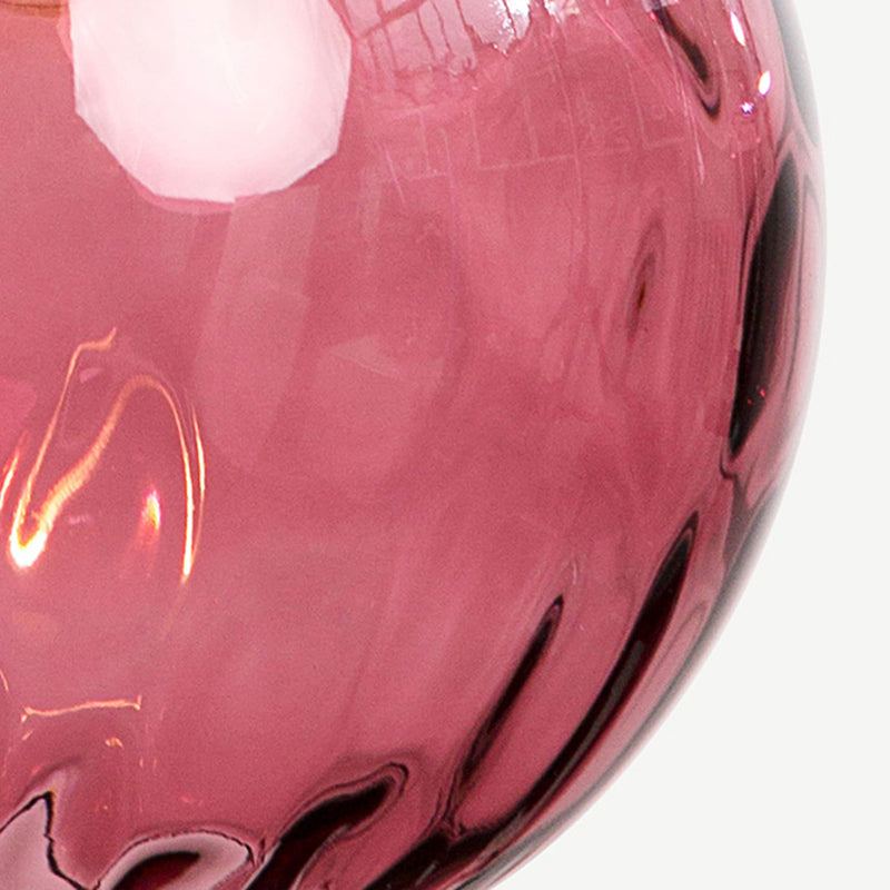 Extreme close-up of the moulded dimples in the plum glass of the Clérachic water ripple globe pendant, lit from inside.
