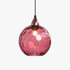 Studio shot of a raspberry-pink Clérachic water ripple glass globe pendant, a copper socket cup at the neck of the dimpled globe.