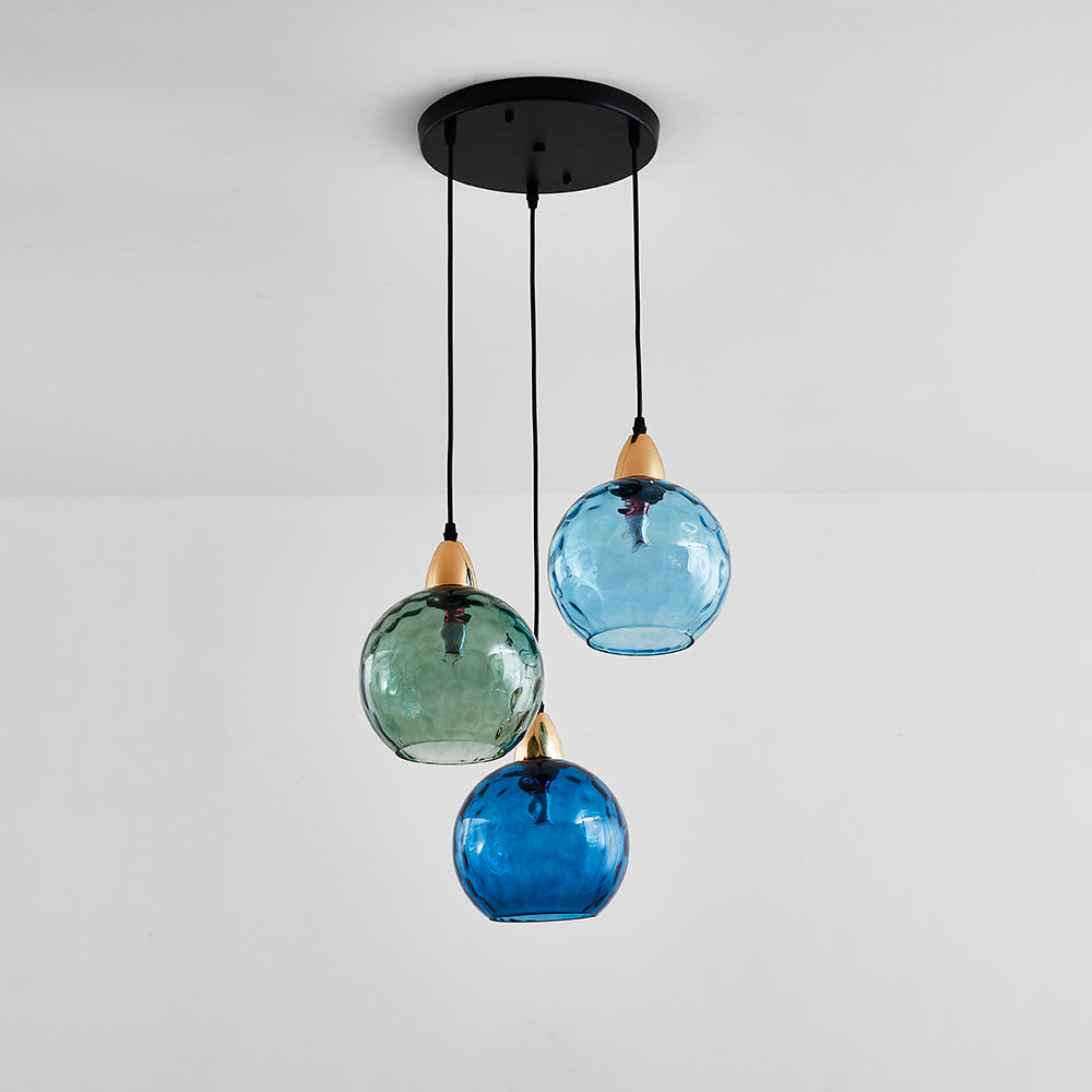Green and blue water-ripple globes on the Clérachic 3-globe cluster pendant, hung from a round black canopy against a pale wall.