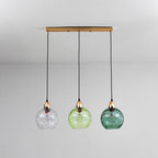 The Clérachic Water-Ripple Glass Pendant Light on its brass bar, clear, light green and teal globes hanging level from the ceiling.