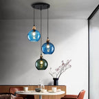 Blue and green ripple globes glowing on the Clérachic cluster pendant above a round dining table set for a meal.