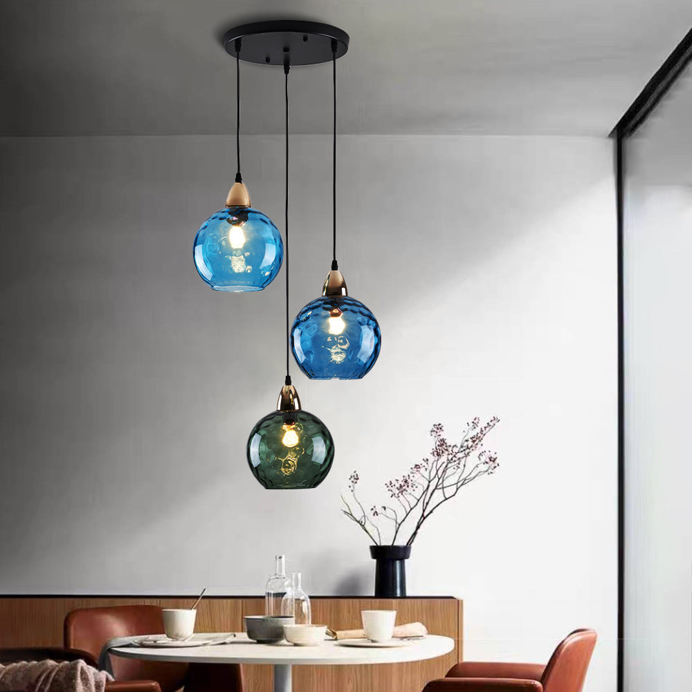 Blue and green ripple globes glowing on the Clérachic cluster pendant above a round dining table set for a meal.