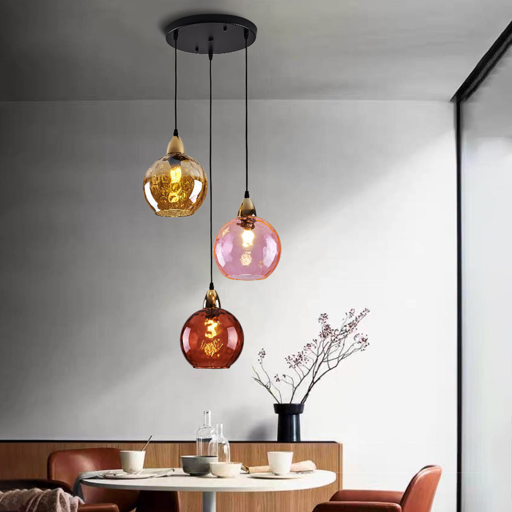 Amber, pink and red ripple globes lit on the Clérachic cluster pendant above a round wooden dining table.
