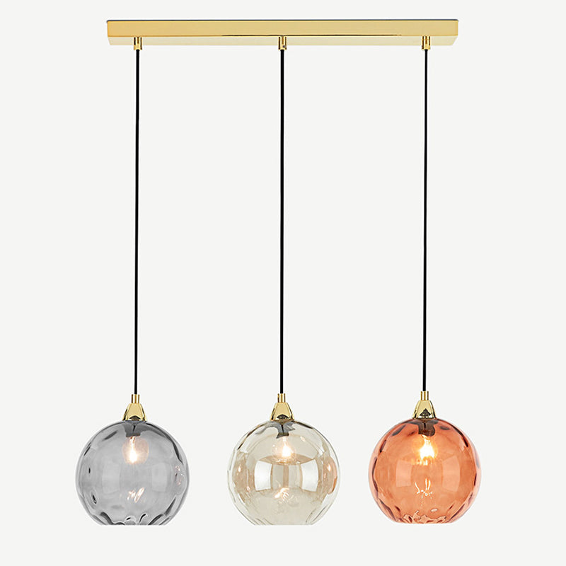 Clérachic ripple-glass pendant on its polished brass bar, smoke, champagne and orange globes hanging level on black cords.