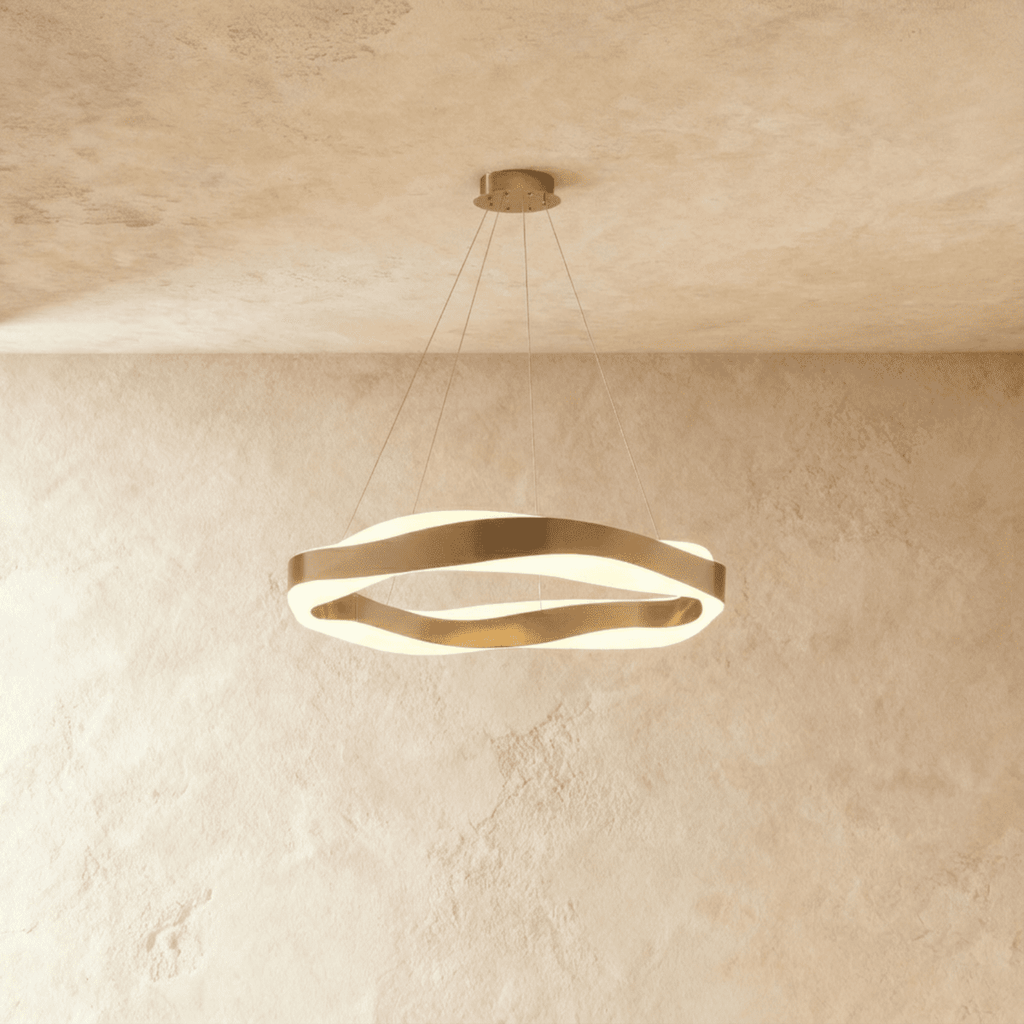 Clérachic gold wave-ring chandelier lit, showing the frosted diffuser glowing between its twisting gold bands.