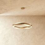 Clérachic gold wave-ring chandelier lit, showing the frosted diffuser glowing between its twisting gold bands.