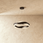 Clérachic round wave chandelier with black twisting bands and a black ceiling plate, lit on a warm plaster wall.
