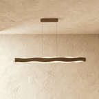 Clérachic longer linear wave pendant in a bronze-toned finish, its frosted light glowing under the wavy band.
