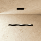 Clérachic black linear wave pendant on two thin cables, its soft frosted LED glow visible below the band.