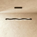 Clérachic long black wavy LED pendant with an oblong black ceiling plate, lit against a limewash wall.