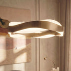 Close view of the Clérachic gold wave-ring chandelier, brushed metal bands crossing over a glowing frosted diffuser.