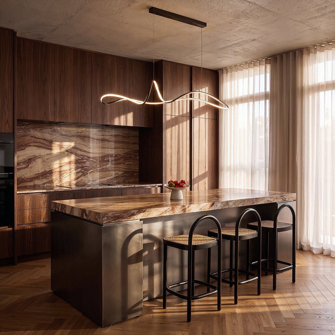 Clérachic black ribbon pendant glowing above a stone-topped kitchen island with cane bar stools and sheer curtains.