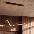 Close view of the Clérachic black ribbon pendant, its LED edge lit warm, under a long bar canopy on a concrete ceiling.