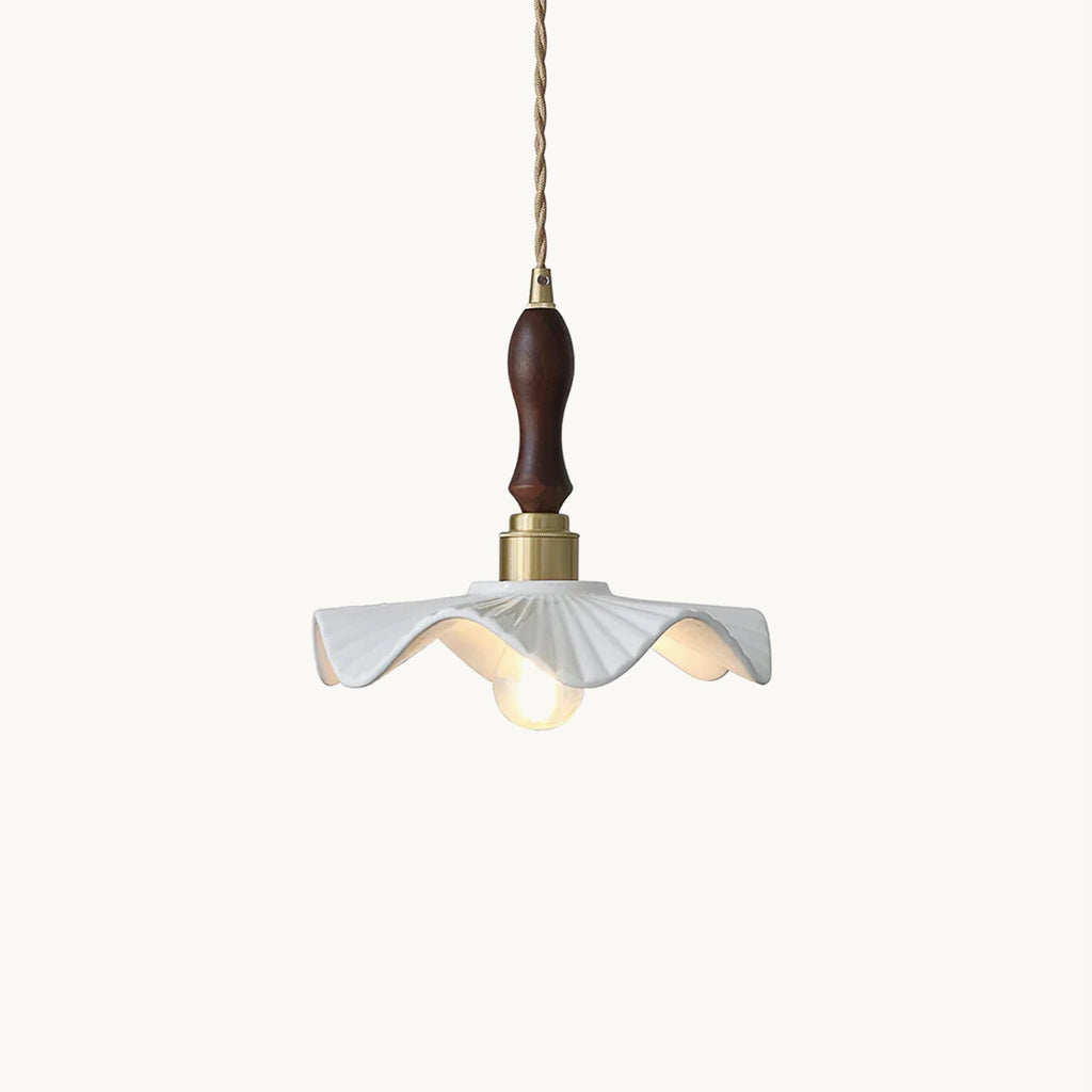 White wavy-edged ceramic shade under a brass socket and a dark carved wooden handle, this Clérachic pendant on a twisted cord against white.